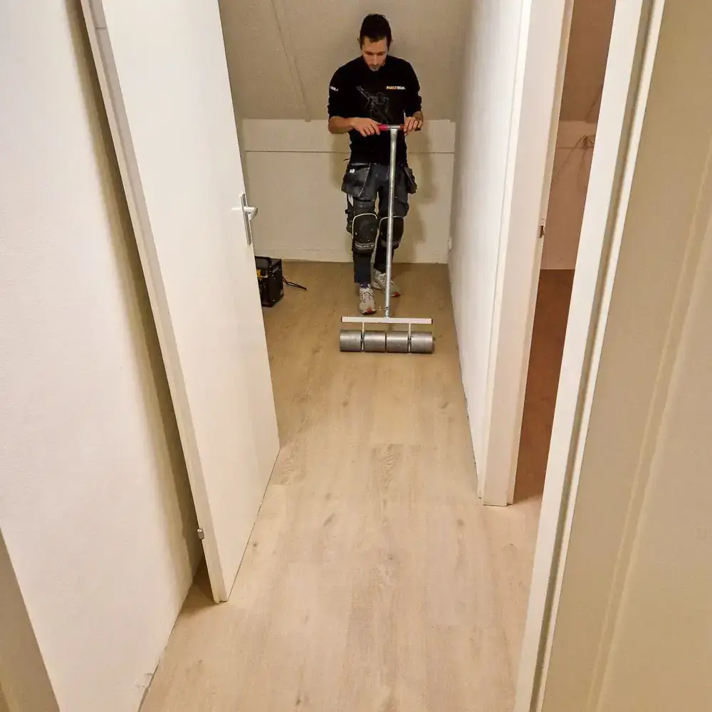 Monteur van Parketreus walst de naden aan van een PVC vloer.
