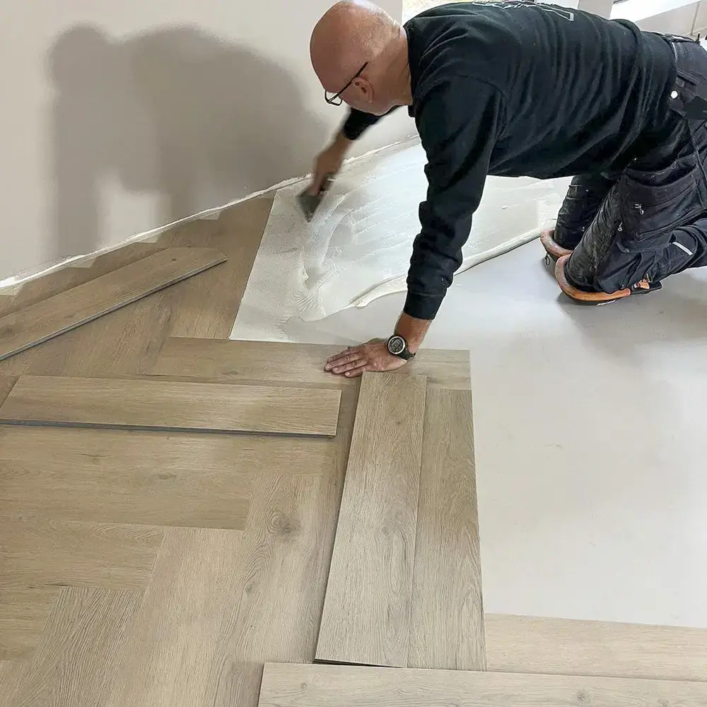 Monteur van Parketreus brengt de lijm aan met een lijmkam voor het monteren van een PVC vloer.