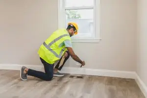 Installateur plaatst strakke witte plint op moderne PVC vloer voor een professionele afwerking - plinten op een pvc vloer voor de juiste afwerking